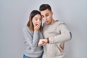 Naklejka premium Young hispanic couple standing over white background looking at the watch time worried, afraid of getting late