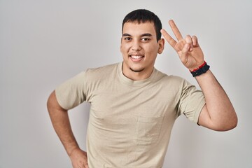 Young arab man wearing casual t shirt smiling looking to the camera showing fingers doing victory...