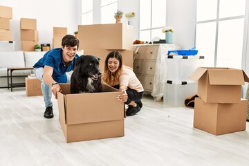 Young caucasian couple smiling happy transporting dog into cardboard box as a car at new home.