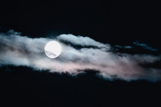 Blurry unfocused Full moon in the night sky hidden behind clouds tinted with sunset light