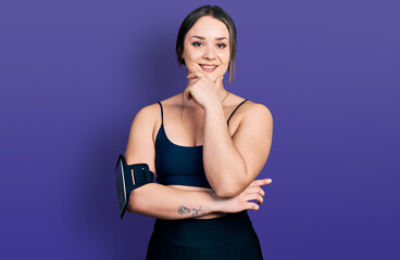 Obraz premium Young hispanic woman wearing sportswear looking confident at the camera smiling with crossed arms and hand raised on chin. thinking positive.