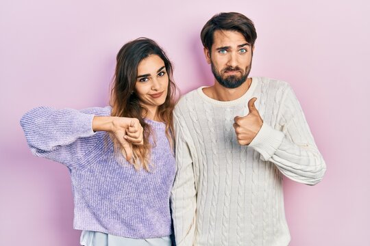 Young hispanic couple wearing casual clothes doing thumbs up and down, disagreement and agreement expression. crazy conflict