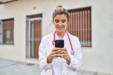 Fototapeta premium Young blonde woman wearing doctor uniform using smartphone at street