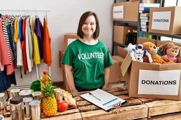 Young down syndrome woman wearing volunteer t shirt at donations stand looking positive and happy...