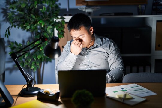 Young chinese man working using computer laptop at night tired rubbing nose and eyes feeling fatigue and headache. stress and frustration concept.