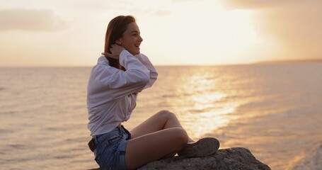 Happy young smiling woman sitting near sea at sunset
