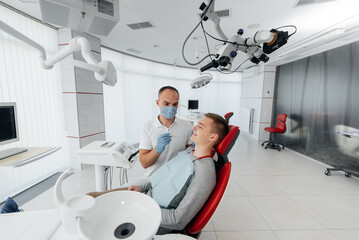 Fototapeta premium A young dentist examines and treats the teeth of a young man in modern white dentistry close-up. Dental prosthetics, treatment and teeth whitening. Modern dentistry. Prevention.
