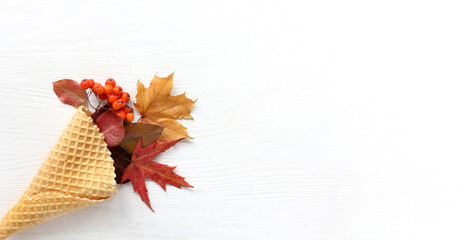 waffle cone with autumn leaves and berries on a light surface top view. seasonal bouquet