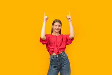 Positive attractive young woman shows something up in empty space isolated on bright yellow background.