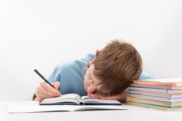 Bored and tired boy doing homework on desk. Schoolboy fell asleep on notebook. Home schooling.