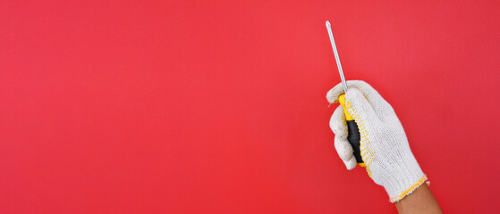 hand wearing white gloves holding standard size yellow flat head screwdriver isolated red background