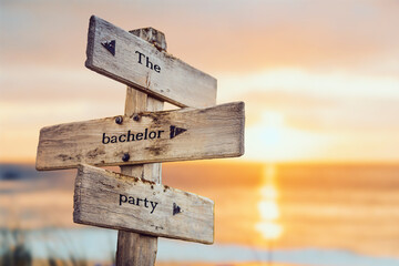 the bachelor party text quote on wooden crossroad signpost outdoors on beach with pink pastel...