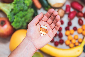Hand holding food supplements over vegetables and fruits for a healty lifestyle