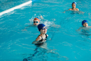 A group of boys and girls play and learn to swim in a modern swimming pool. Development of children's sports. Healthy parenting and promotion of children's sports.