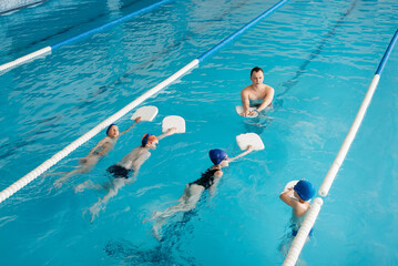 A group of boys and girls train and learn to swim in a modern swimming pool with an instructor....