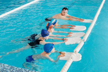 A group of boys and girls train and learn to swim in a modern swimming pool with an instructor. Development of children's sports. Healthy parenting and promotion of children's sports.