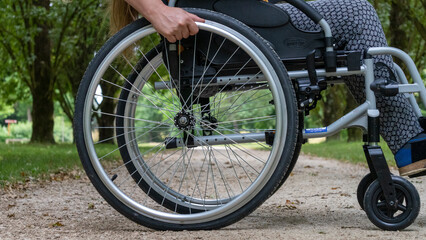 Close-up of a wheelchair in profile, a young woman sitting on it, in the middle of nature