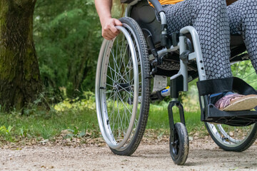Close-up of a wheelchair from the front, a young woman sitting on it, in nature
