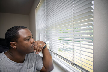 Sad and depressed man at home looking through bedroom window
