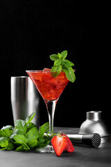 Cold summer strawberry cocktail mojito, margarita, daiquiri in a martini glass. Fresh strawberry drink with ice, bartender tools set and mint leaves on dark background. Iced strawberry lemonade