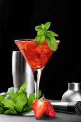Cold summer strawberry cocktail mojito, margarita, daiquiri in a martini glass. Fresh strawberry drink with ice, bartender tools set and mint leaves on dark background. Iced strawberry lemonade