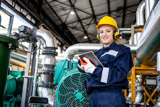 Portrait of female caucasian power plant worker standing by generators and gas pipes.