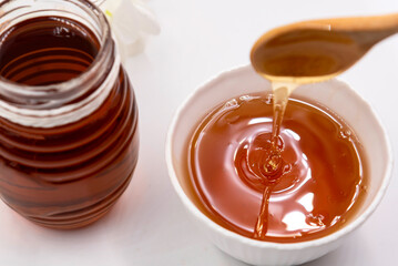 fresh pure honey in glass bowl with honey dripper on wooden tray.