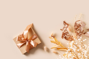 Gift box with golden ribbon and dry grass and flowers on beige background
