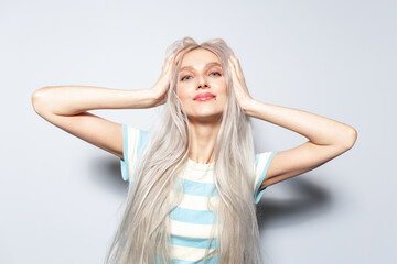 Fototapeta premium Portrait of cute blonde girl holding hands on head, on white background.