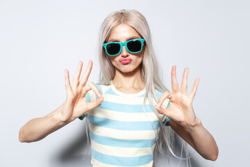 Portrait of funny blonde girl showing ok gesture with hands on white background.