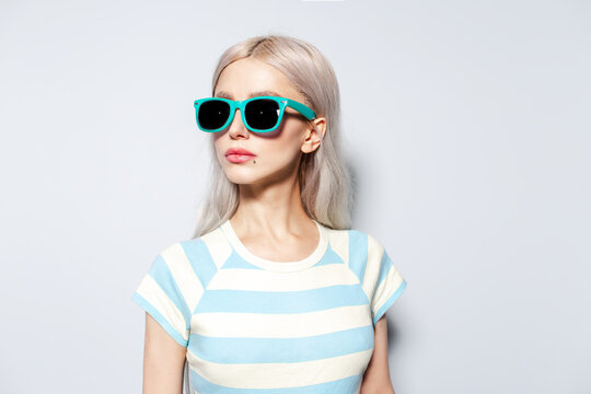Portrait of fashionable blonde girl in striped shirt wearing sunglasses on white.