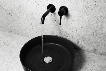 Close-up of black sink and wall mounted faucet with flowing water.