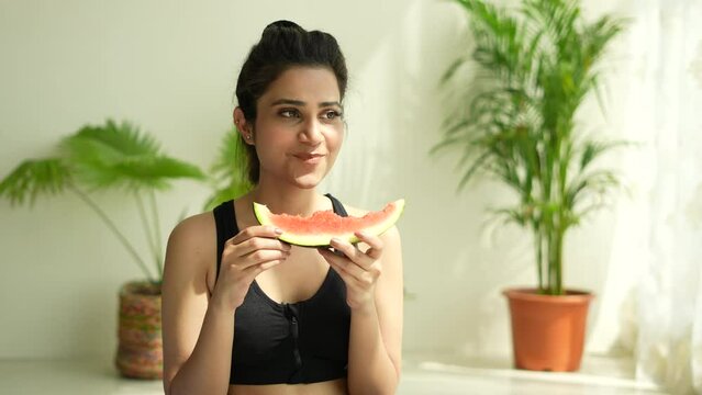 A young Indian woman eating a slice of watermelon and smiling after yoga. Summer and lifestyle concepts.good health.female fitness.closeup camera. 
