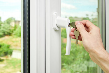 A man locks or unlocks a plastic window with keys