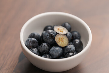 Fresh blueberries in white bowl one berry is cut in halves