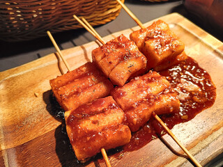 Tteokbokki with sausage in spicy sauce (Korean rice cake skewers) on wooden board, Korean food style