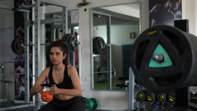  A Young Indian fit  girl exercising in gym, doing power sit-ups with weights. Determined woman doing crossfit work out to complete challenge.