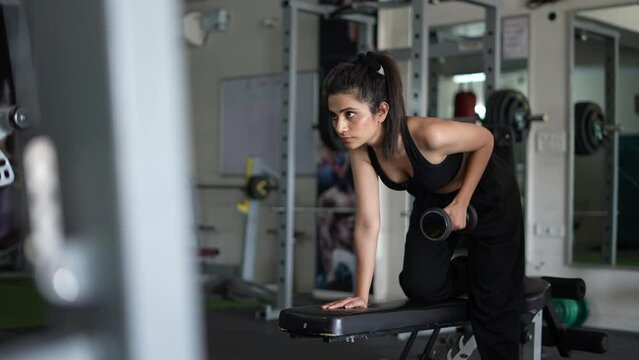 A young Indian girl hands taking bodybuilding dumbbells in gym club. Asian woman hands taking weight lifting in gym. Fitness girl having sport training in fitness gym.
