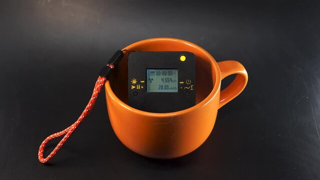 Large ceramic mug of bright orange color. Inside is a radiation dosimeter. The concept of measuring and sanitary control of health safety. Exceeding the permissible radiation