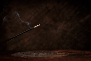 Lit incense on rustic dark wood background. Spiritual atmosphere, space for text.
