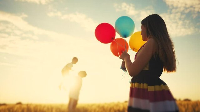 happy family celebrates birthday in the park. girl a holding colorful balloons silhouette in the field. dad throws his son into the sky in lifestyle the park. happy family kid dream concept