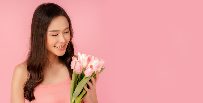 Portrait attractive asian women holding flowers or tulip flower Beautiful girl looking at flower with smile face Copy space isolated over pink pastel color background International Women's Day