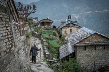 Man walking with a stick through the old Himalayan town of Ghandruk in Nepal, Asia