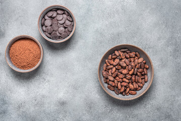 Cocoa beans, cocoa powder and chocolate in bowls on grunge gray background. Top view