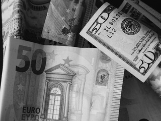Paper banknotes in denominations of 50 dollars and 50 euros, a close-up shot. Black and white image.