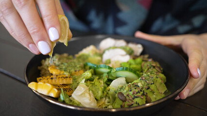 Woman squeezes fresh juice from lemon slice into dish. Healthy salad bowl with porridge avocado and turkey seasoned with fresh lemon juice closeup