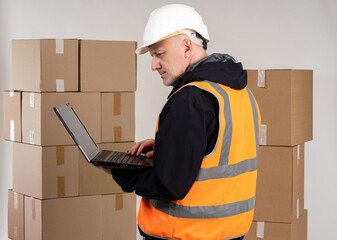 Warehouse manager. Man with laptop in front of boxes. Warehouse manager in protective hard hat....