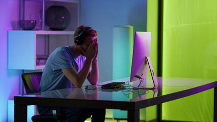 Sad guy losing computer game in neon room. Frustrated gamer feeling stressed