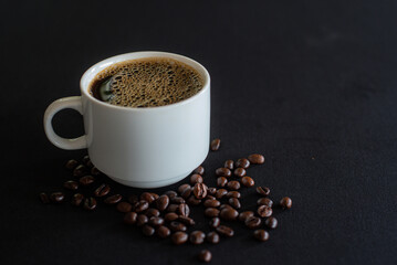 Cup full of coffee with bubbles and black coffee beans on black background.