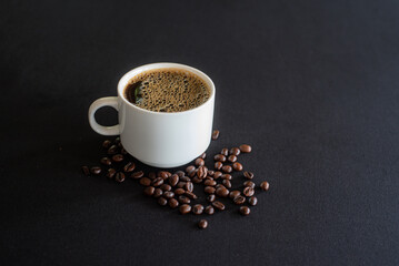 Cup full of coffee with bubbles and black coffee beans on black background